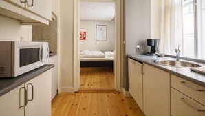Una cucina compatta con forno a microonde, macchina del caffè e lavello. Si intravede un letto attraverso una porta aperta sullo sfondo.