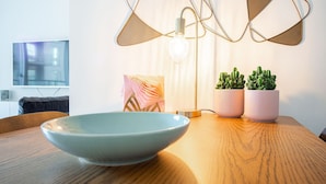 Et moderne spiseområde med et træbord, en blå skål, en gulvlampe og to krukker med planter.