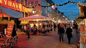 Een geplaveid straatje met winkels en terrassen, met een bordje waarop 'NYHAVN 17' staat.