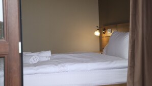 Uma cama bem arrumada com roupa de cama branca, um abajur e uma cabeceira de madeira.