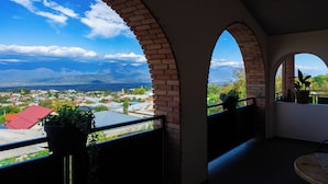 Uma varanda com arcos de tijolo, um vaso com planta e vista para uma cidade e montanhas.