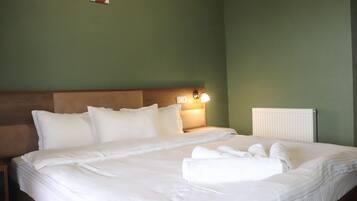 Ein ordentlich gemachtes Bett mit weißen Bettwäsche und Kissen, eine Nachttischlampe und ein Heizkörper an der Wand.