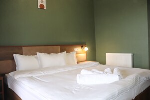 Una cama bien tendida con sábanas y almohadas blancas, una lámpara de noche y un radiador en la pared.