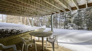 Une terrasse en bois à l’extérieur, avec une table et des chaises, entourée d’un paysage enneigé et d’arbres.