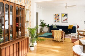 Een woonkamer met een donkerblauwe bank, een houten kast en potplanten.