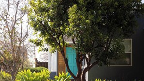 Ein Haus mit einer türkisblauen Tür, umgeben von üppigem Grün und einem Baum.
