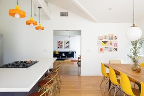 Een moderne keuken met een centraal eiland, barkrukken en een eethoek met gele stoelen.