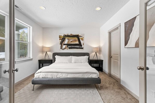 A modern bedroom with a large bed, two bedside tables, a floor lamp, and artwork on the walls.