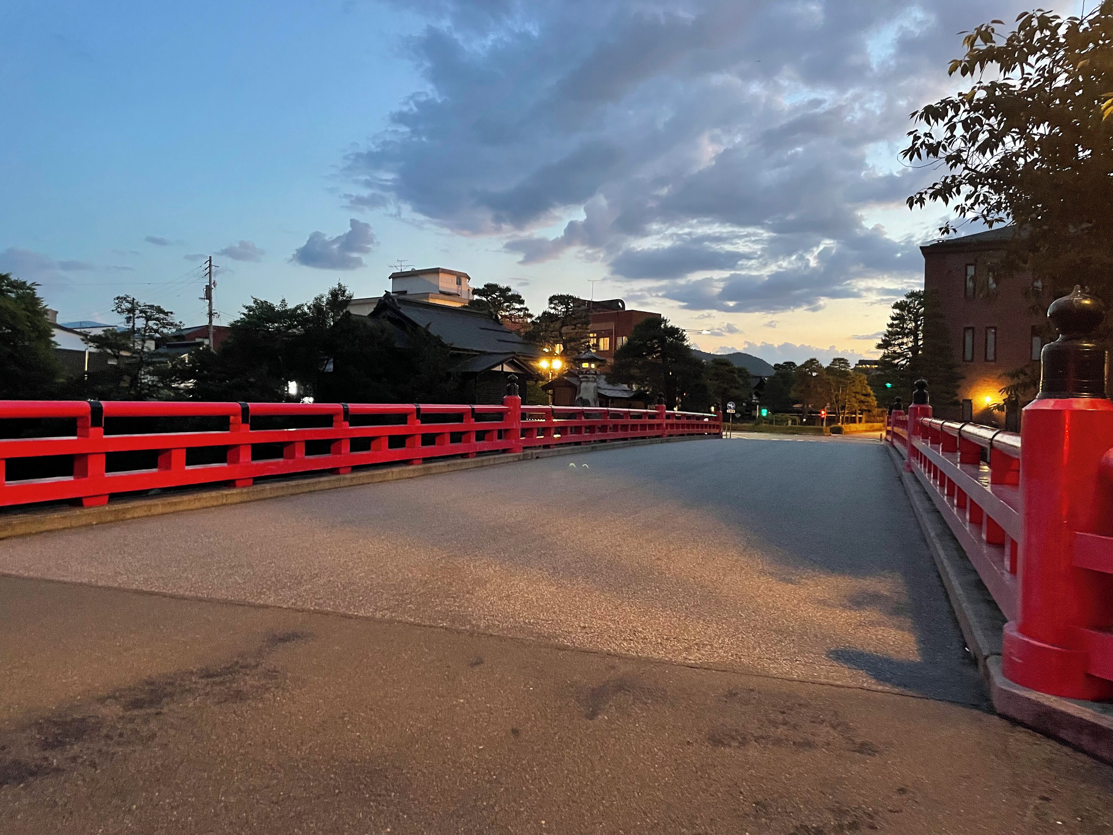 A bridge with red railings and street lamps, leading to a building with traditional architecture.