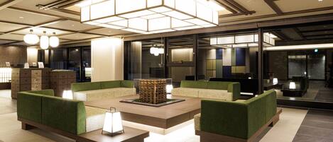 A modern lobby with green upholstered seating, a central coffee table, and a unique geometric light fixture.