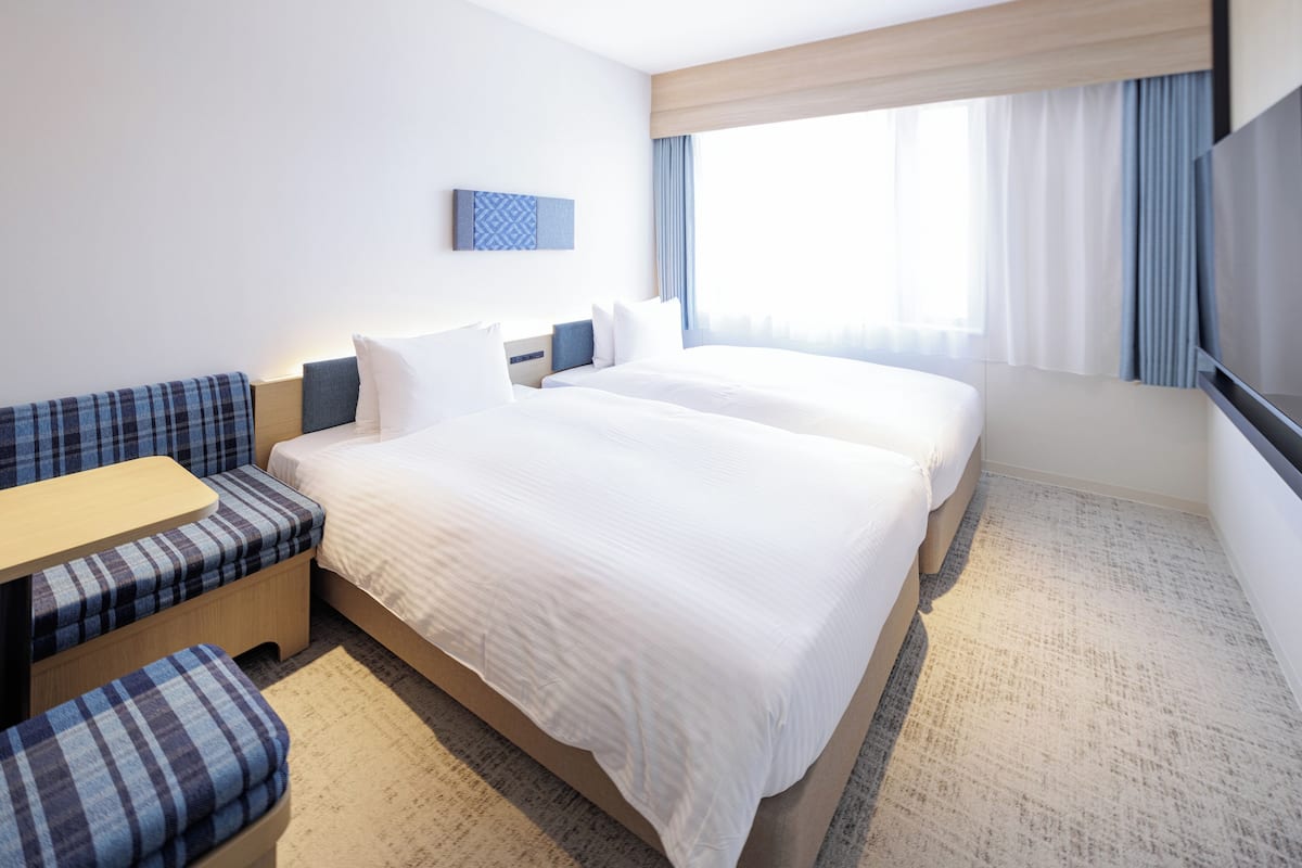 Ett hotellrum med två sängar, en soffa, ett litet bord och en TV.