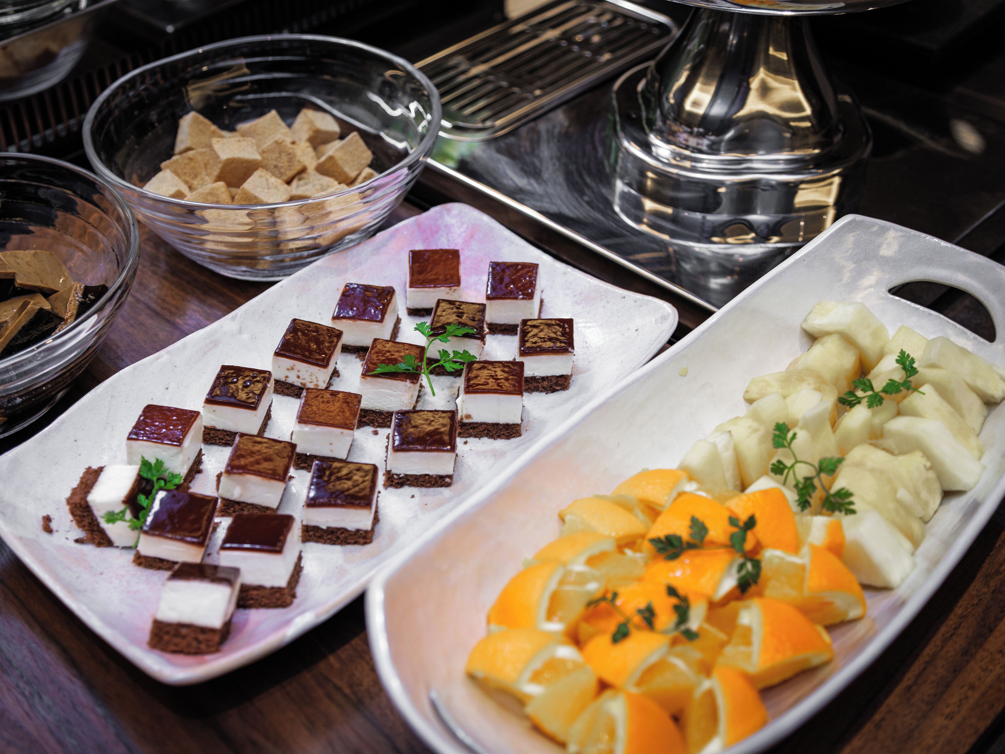 A buffet table with various food items, including desserts and fruit.