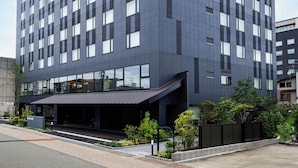 Un hotel moderno con un llamativo letrero de AMANEK en la fachada, con una cuadrícula de ventanas y un área de acceso cubierta.