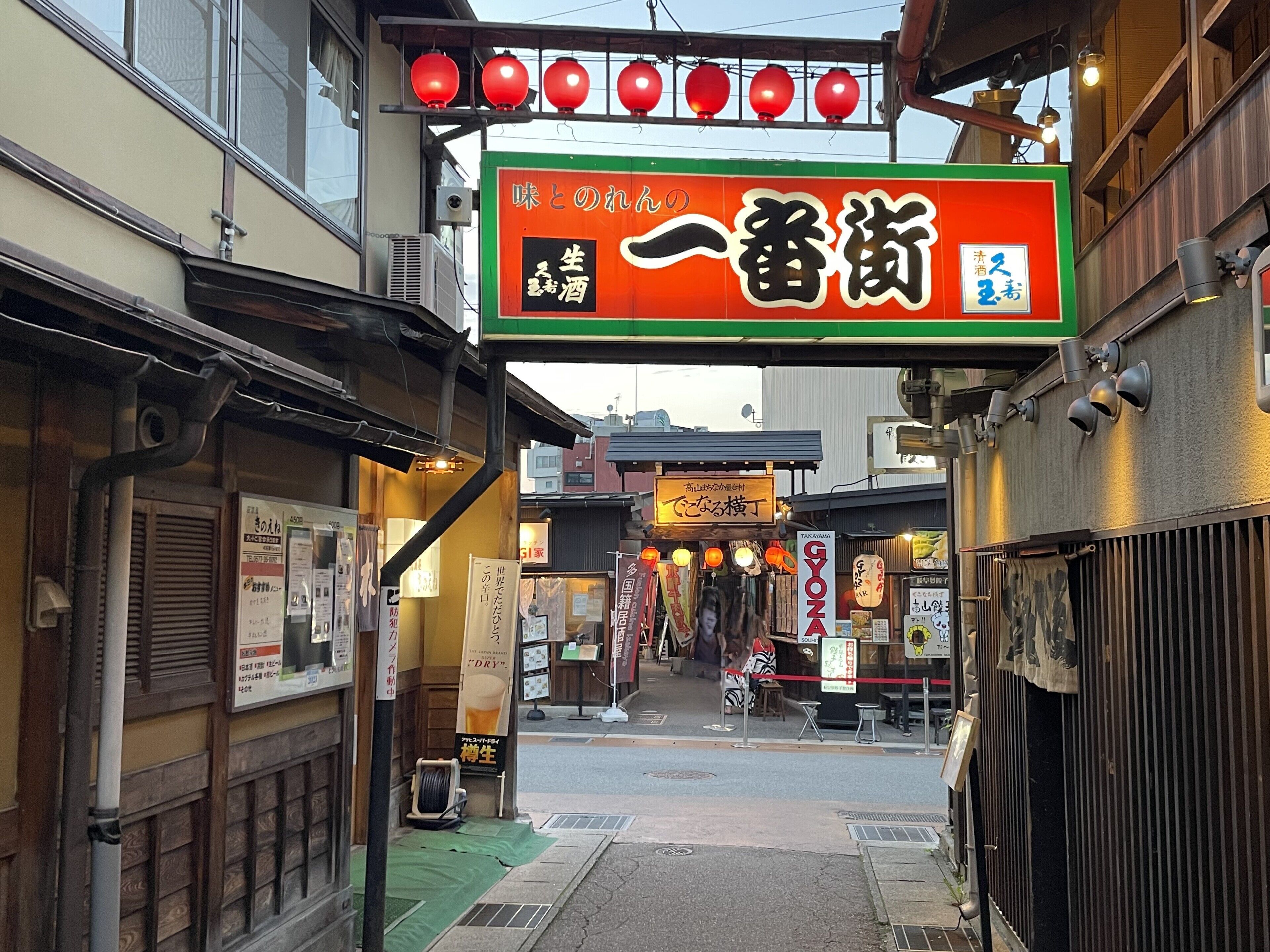 Una calle estrecha con arquitectura japonesa tradicional, que incluye edificios de madera y señalización en japonés.