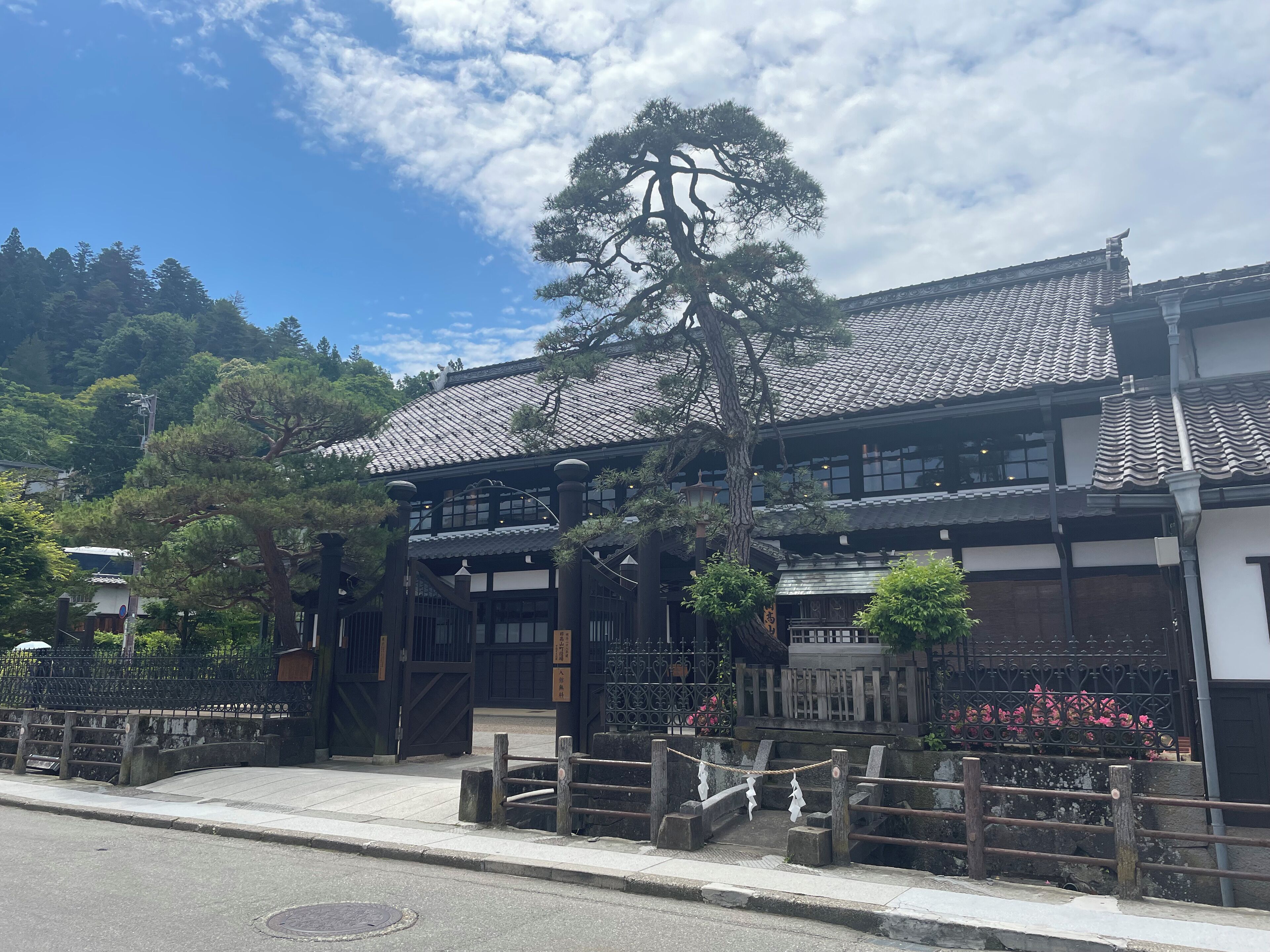 A traditional Japanese building with a tiled roof, wooden structure, and a large tree in front.