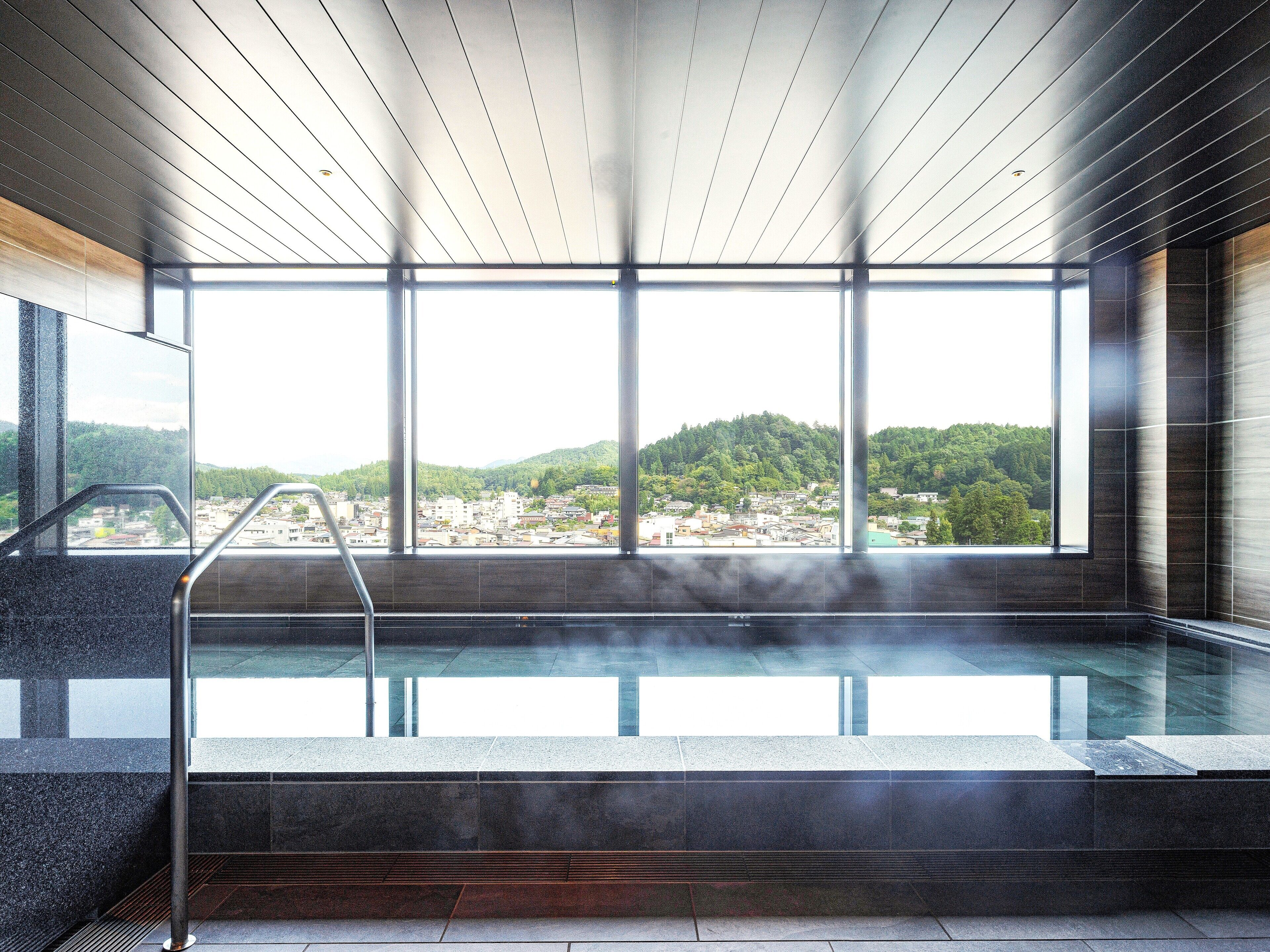 A modern indoor swimming pool with a view of a cityscape and hills.