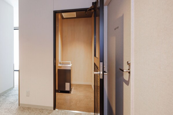 A hotel room with a wooden wardrobe, a small table, and a trash bin. - HOTEL AMANEK HidaTakayama (Takayama)