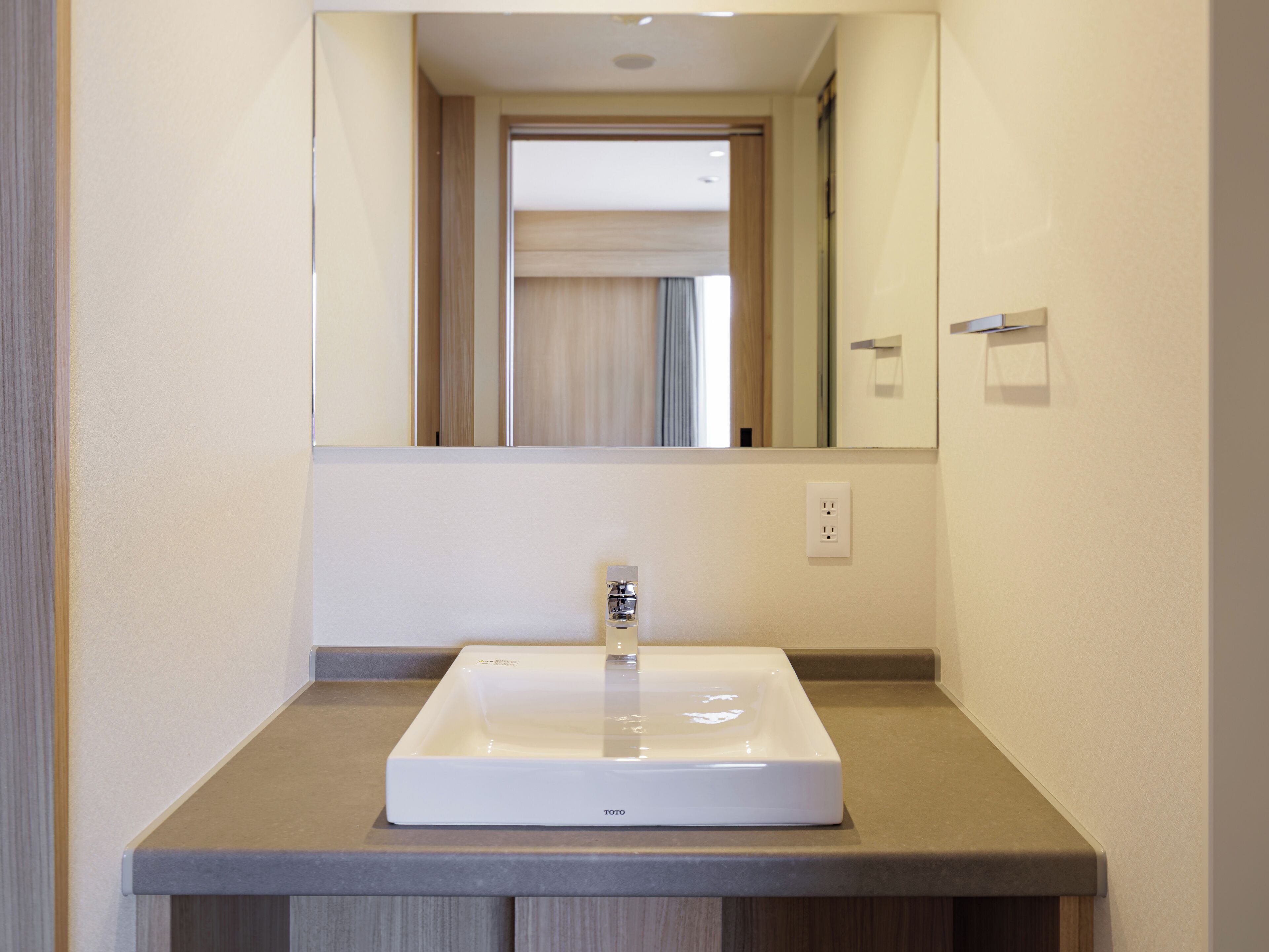 Een badkamer met een witte wastafel, een spiegel erboven en een lichtschakelaar aan de muur.