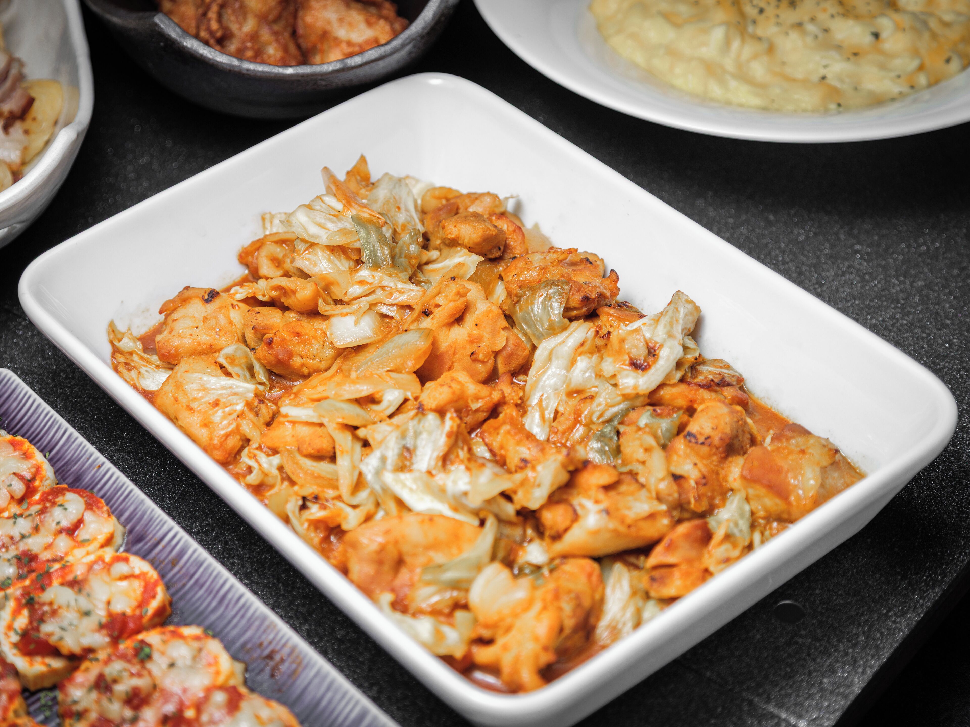 A white rectangular dish filled with a chicken and cabbage casserole, surrounded by other dishes on a dark countertop.
