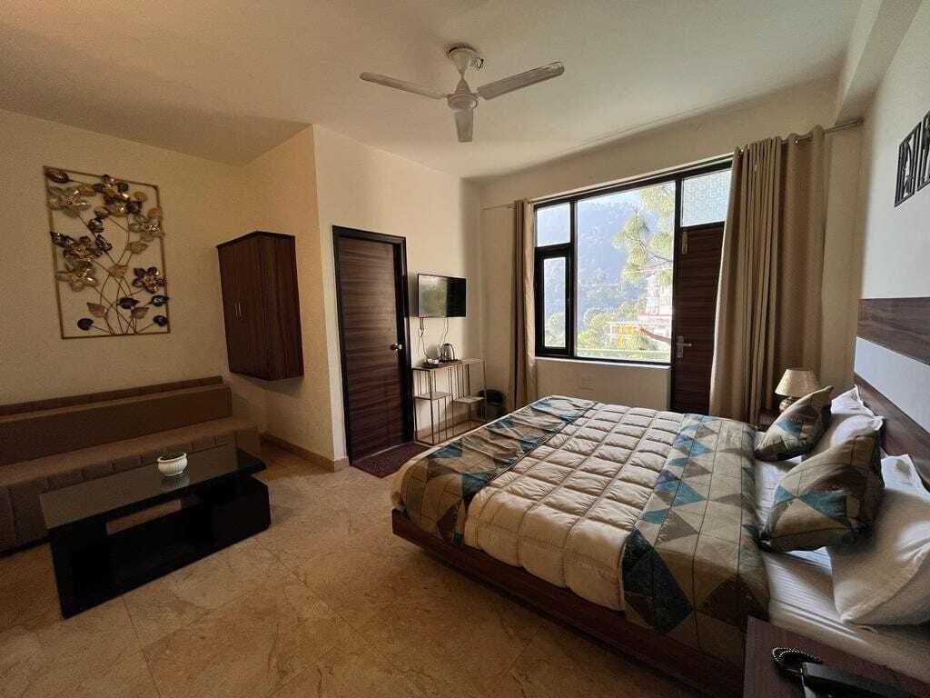 A bedroom with a bed, a desk, a chair, a TV, and a window with curtains.