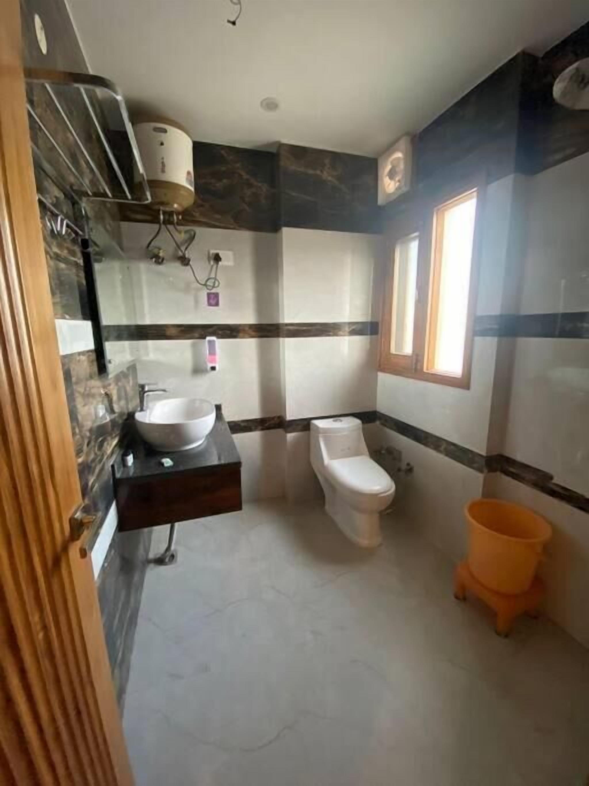 A bathroom with a marble floor, a white sink, a toilet, and a window.