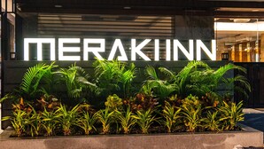 Ein Hotel Eingang mit dem Schriftzug 'MERAKINN' in großen Lettern, umgeben von üppigem Grün.