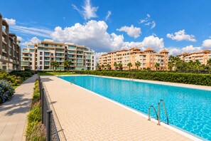 A swimming pool with a tiled deck, surrounded by modern buildings with multiple floors and balconies.