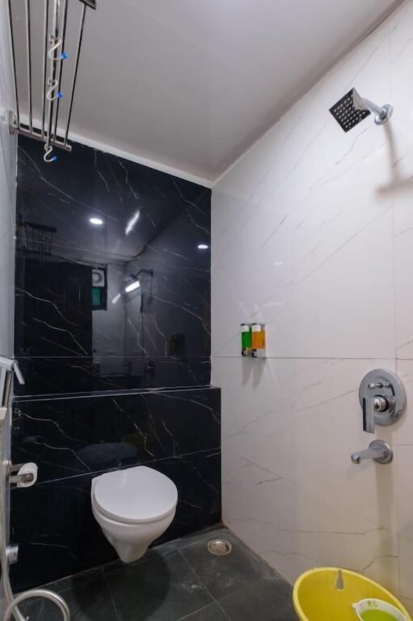 A bathroom with a toilet, a shower, and a yellow bucket.