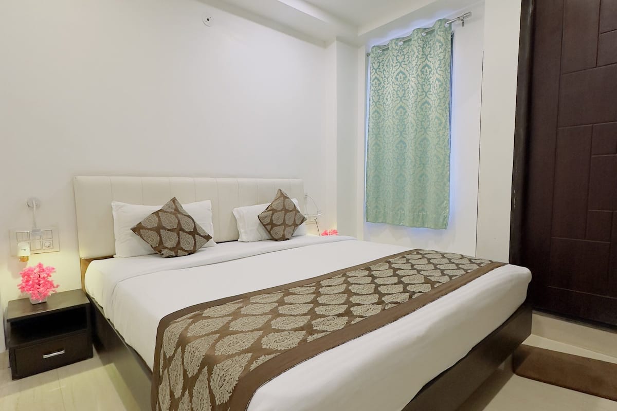 A neatly arranged bedroom with a bed, a bedside table with a lamp, and a window with curtains.