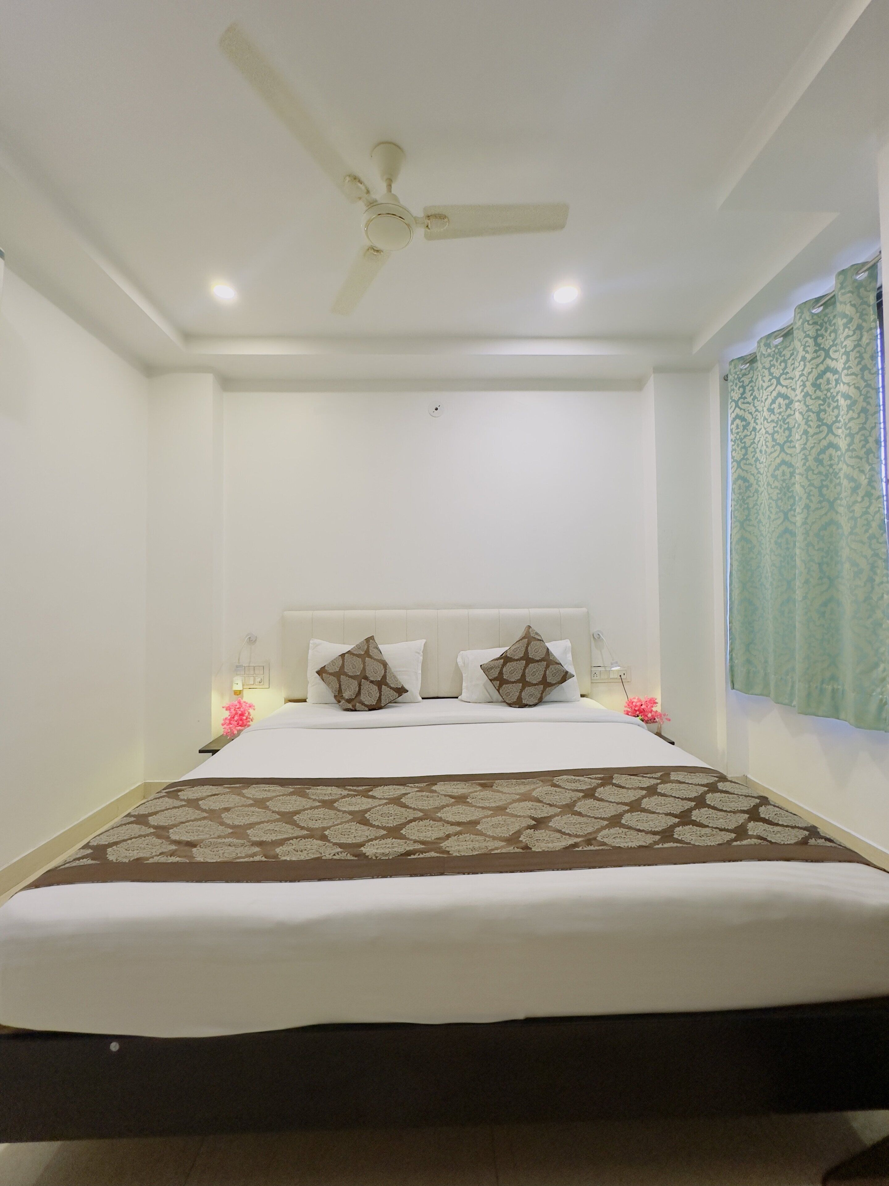 A bedroom with a bed, pillows, a ceiling fan, and a window with curtains.