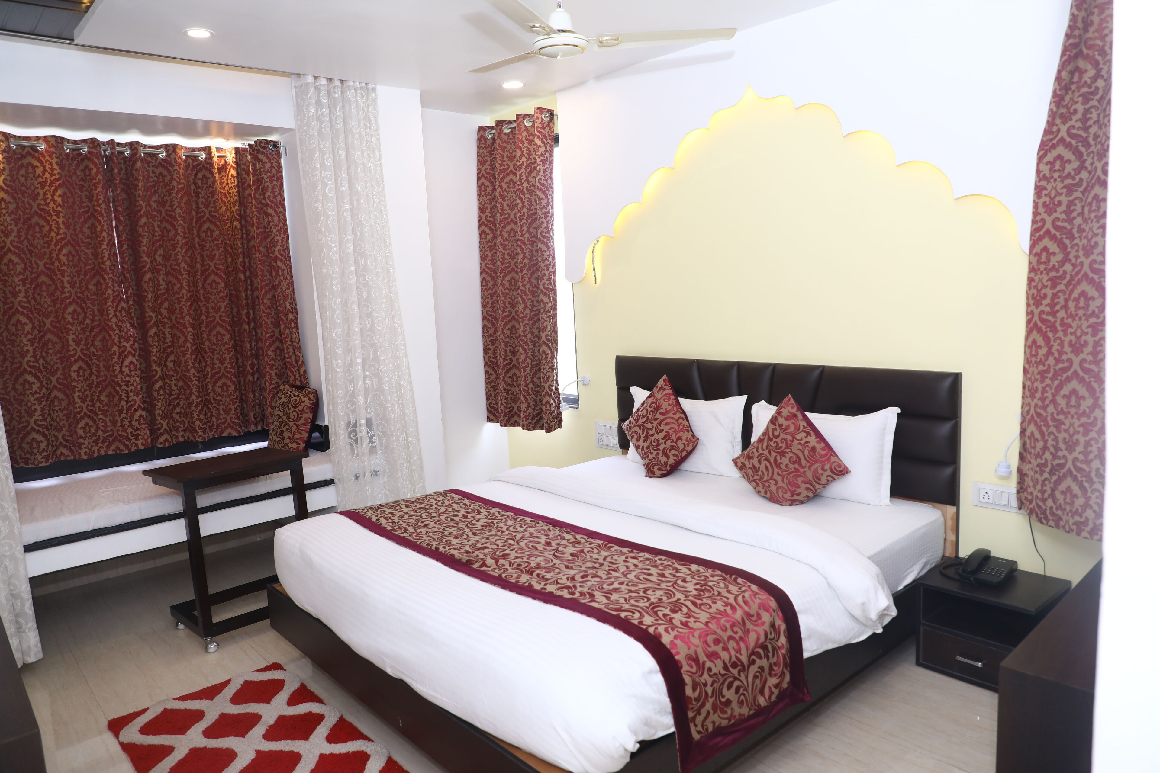 A hotel room with a large bed, a bedside table, a desk, and a ceiling fan.