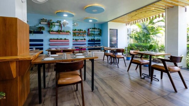 A restaurant with wooden tables and chairs, blue ceiling lights, and potted plants on the walls. - Satkar Retreat (Udaipur)