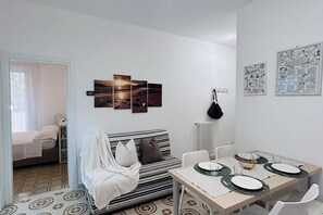 A modern living room with a striped sofa, a dining table set with plates and glasses, and a wall with framed artwork. - Angiolieri Flexrent - Abyssinia (Riccione)