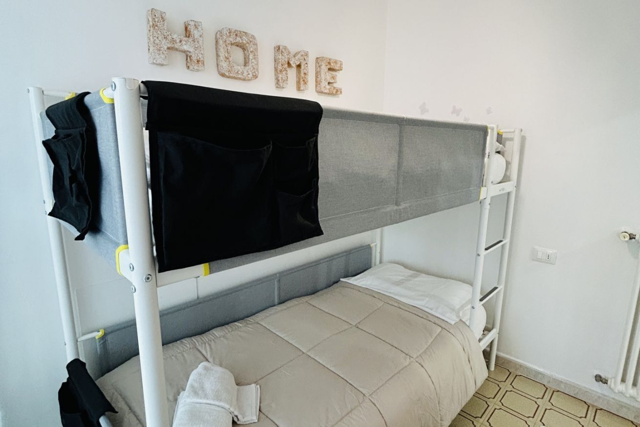 Un lit superposé avec un matelas noir et gris, une couette beige et un oreiller blanc.