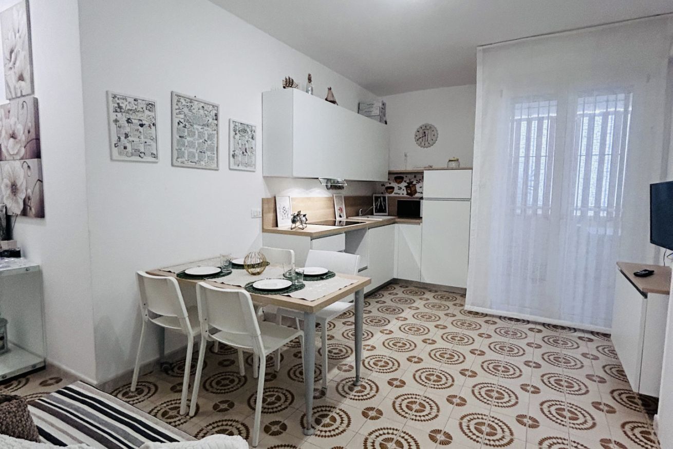 Una cucina compatta con mobili bianchi, un tavolo da pranzo con sedie e piastrelle a motivi.