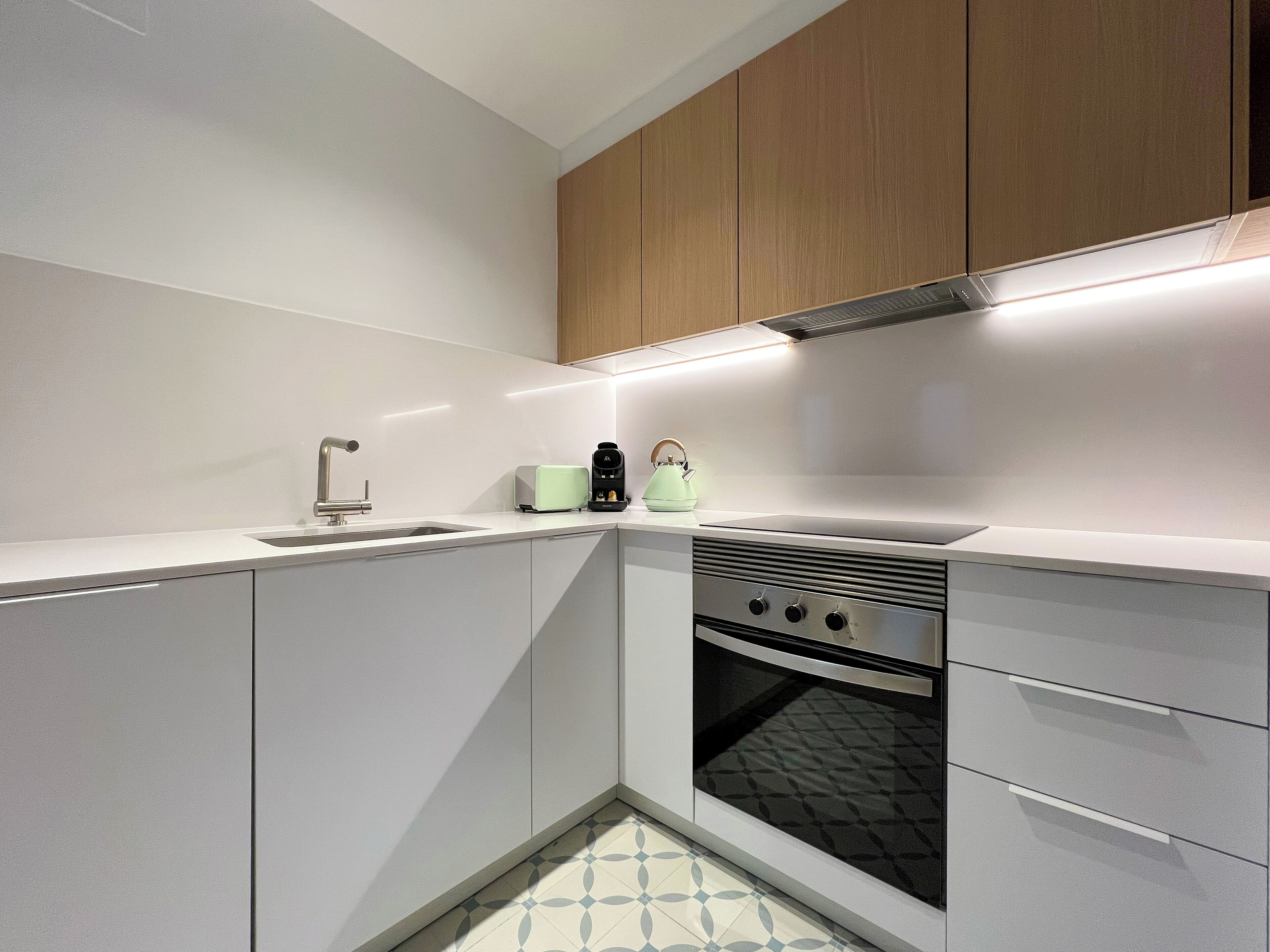 Una cocina moderna con armarios blancos, horno empotrado y cafetera sobre la encimera.
