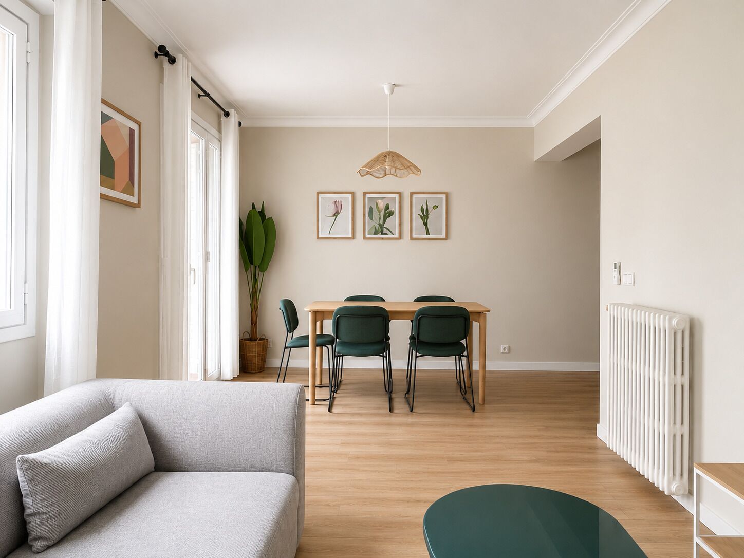 Een moderne woonkamer met een bank, een eettafel met stoelen, een potplant en lijstjes met foto’s aan de muur.