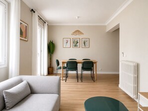 Een moderne woonkamer met een bank, een eettafel met stoelen, een potplant en lijstjes met foto’s aan de muur.