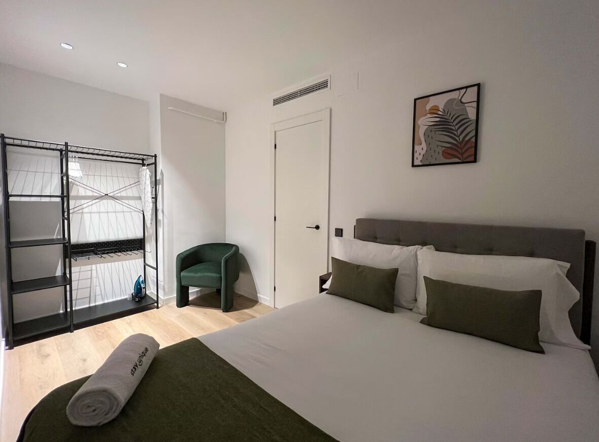 A bedroom with a bed, a green chair, a wardrobe, and a door.