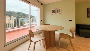 Ein modernes Wohnzimmer mit einem runden Holztisch und zwei Stühlen, ein Balkon mit Blick auf Gebäude und Bäume sowie zwei gerahmte Bilder an der Wand.