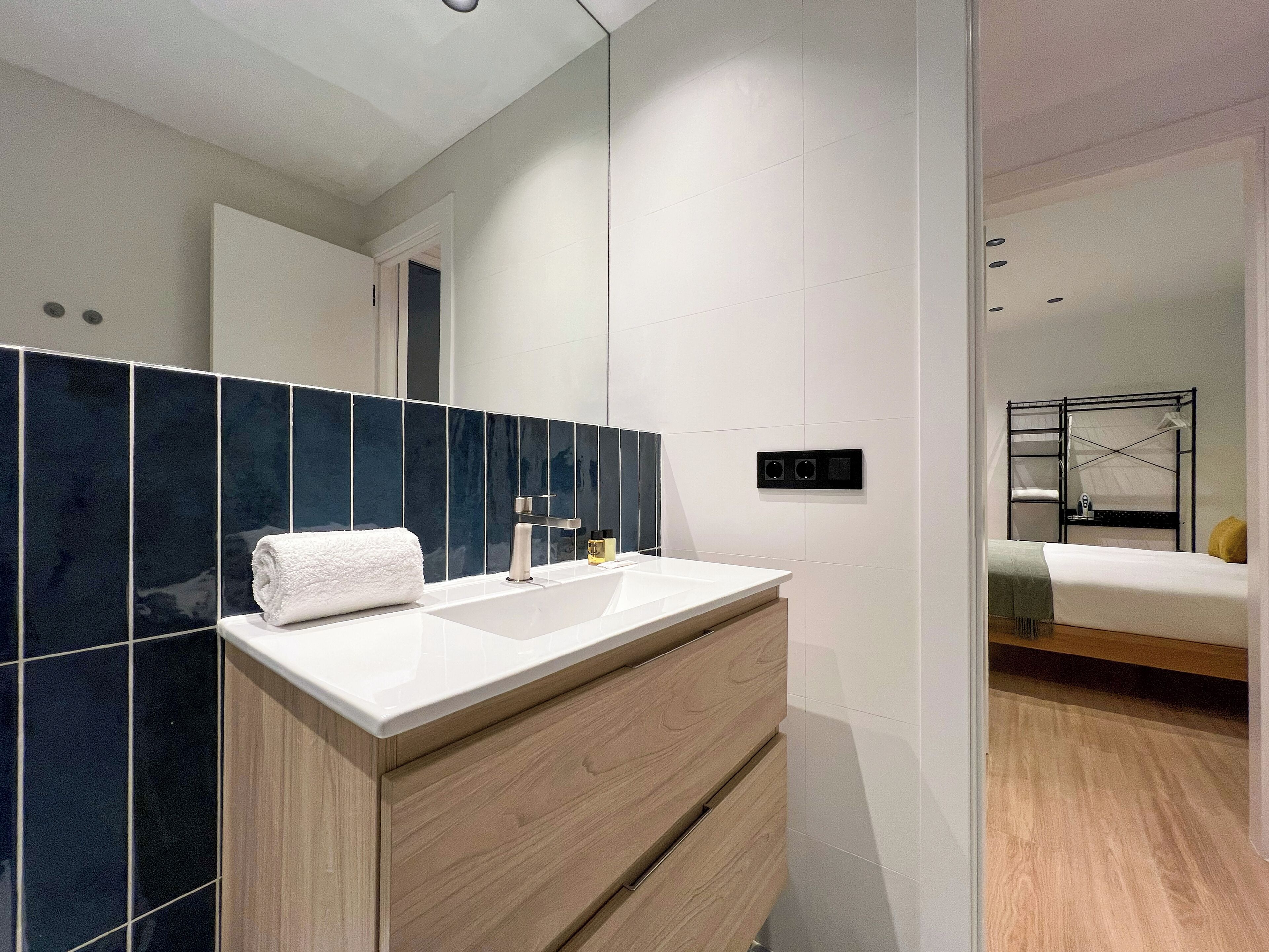 A modern bathroom with a white sink, dark blue tiles, and a wooden vanity.