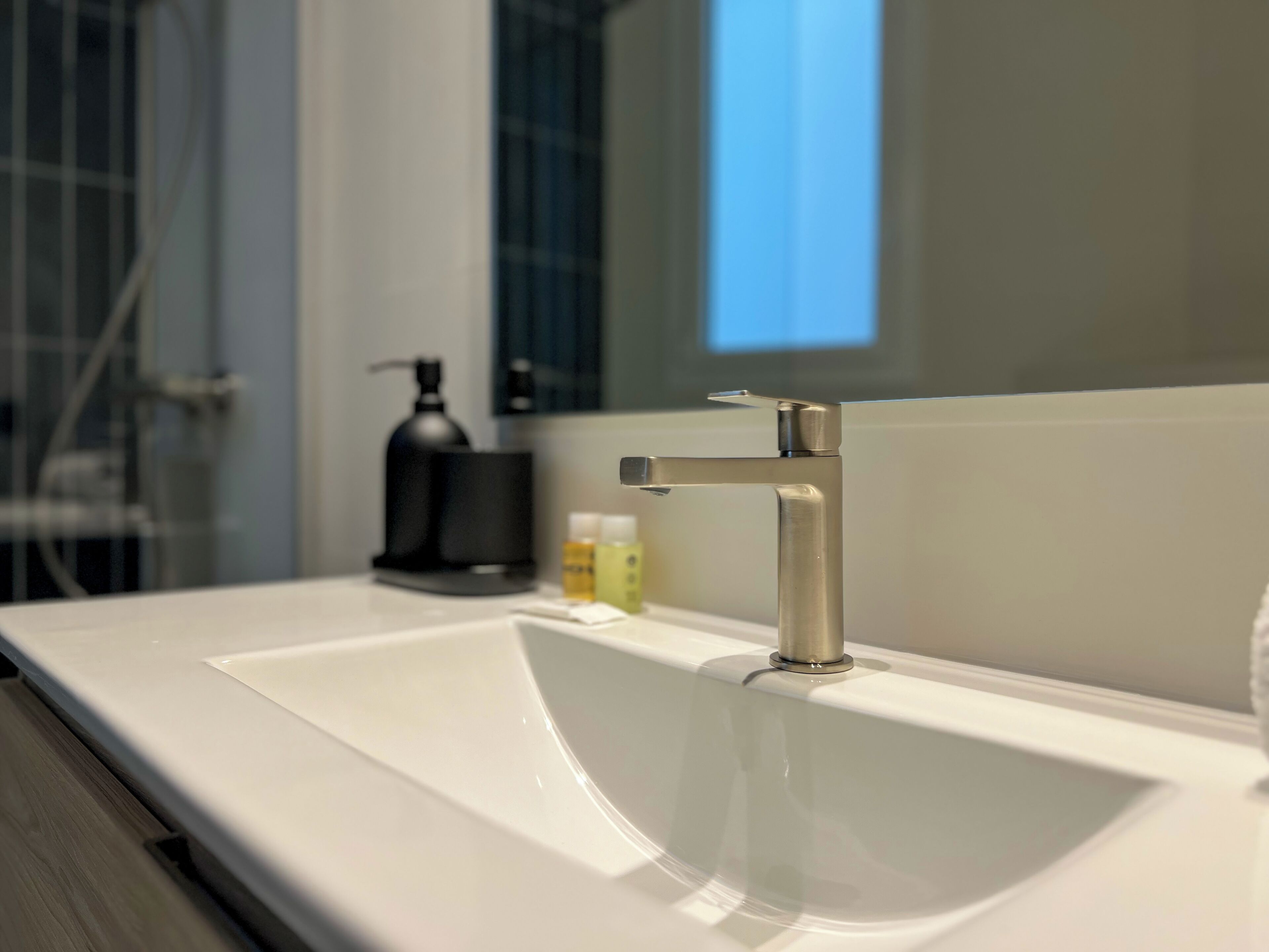 Un baño con lavamanos blanco, un grifo moderno y una botella de jabón para manos.