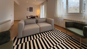 Ein modernes Wohnzimmer mit grauem Sofa, einem gemusterten Teppich und einem Essbereich mit Tisch und Stühlen.