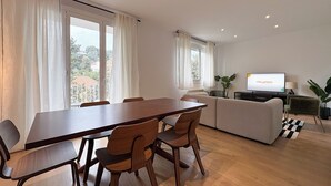 Ein modernes Wohnzimmer mit Essbereich, großen Fenstern, einem Flachbildfernseher und einer Couch.