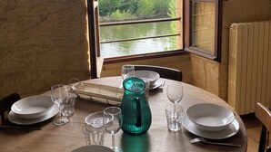 A dining table set for two with a view of a river and hills through an open window.