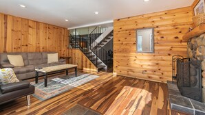 A log cabin interior with a wooden staircase, a sofa, a coffee table, and a fireplace. - Trailside Tahoe Townhouse (Tahoe city)