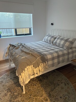 Een slaapkamer met een bed, een raam, een nachtkastje en een vloerkleed.