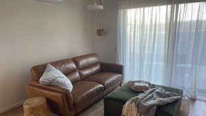 Ein braunes Ledersofa mit Kissen, ein grüner Hocker mit Decke, ein Holzschemel und ein Korbwäscher auf einem Webteppich.