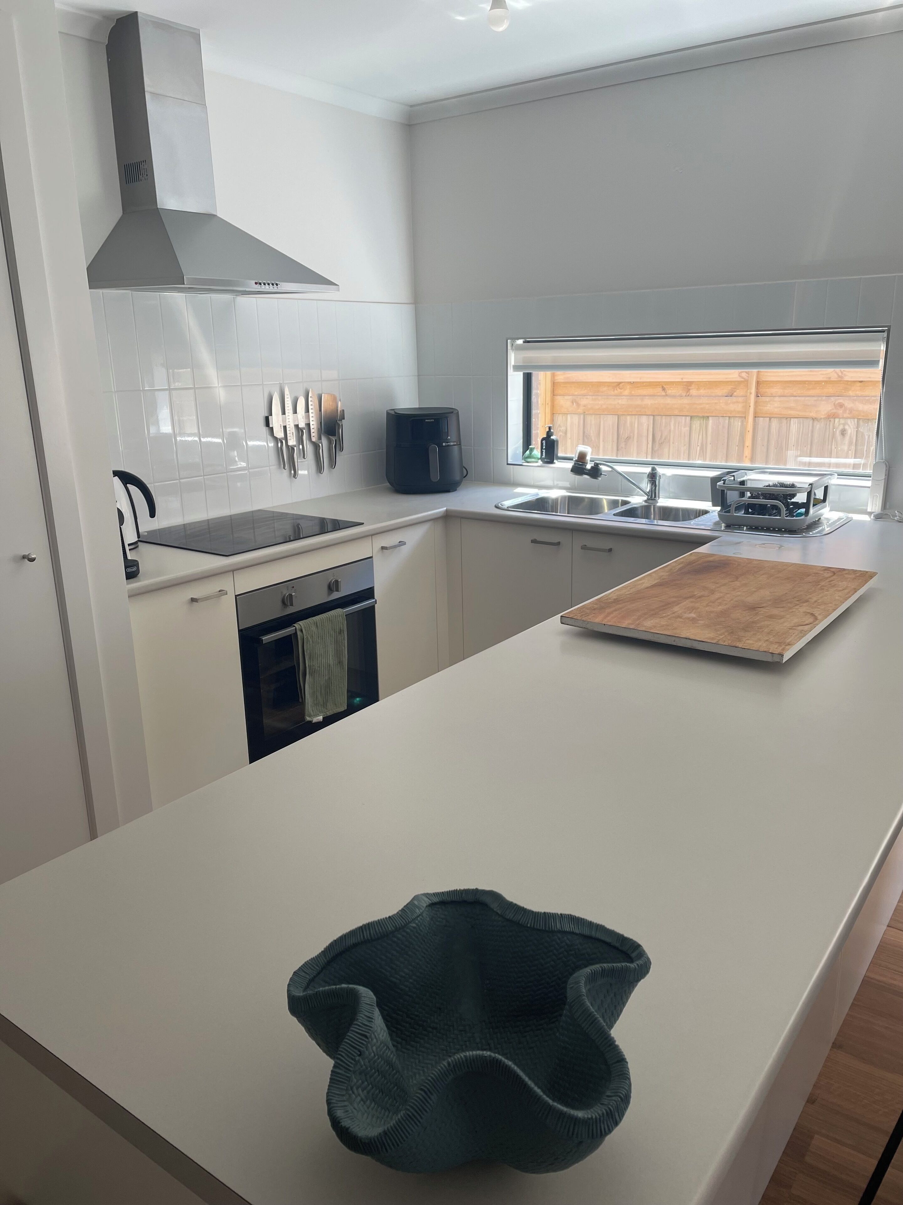 Een moderne keuken met witte kastjes, een roestvrijstalen afzuigkap, een inbouwoven en een groot kookeiland met een snijplank.
