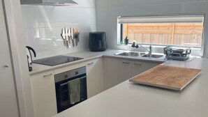 Eine moderne Küche mit weißen Schränken, einer Edelstahl-Dunstesse, einem Einbauofen und einer großen Kochinsel mit Schneidebrett.